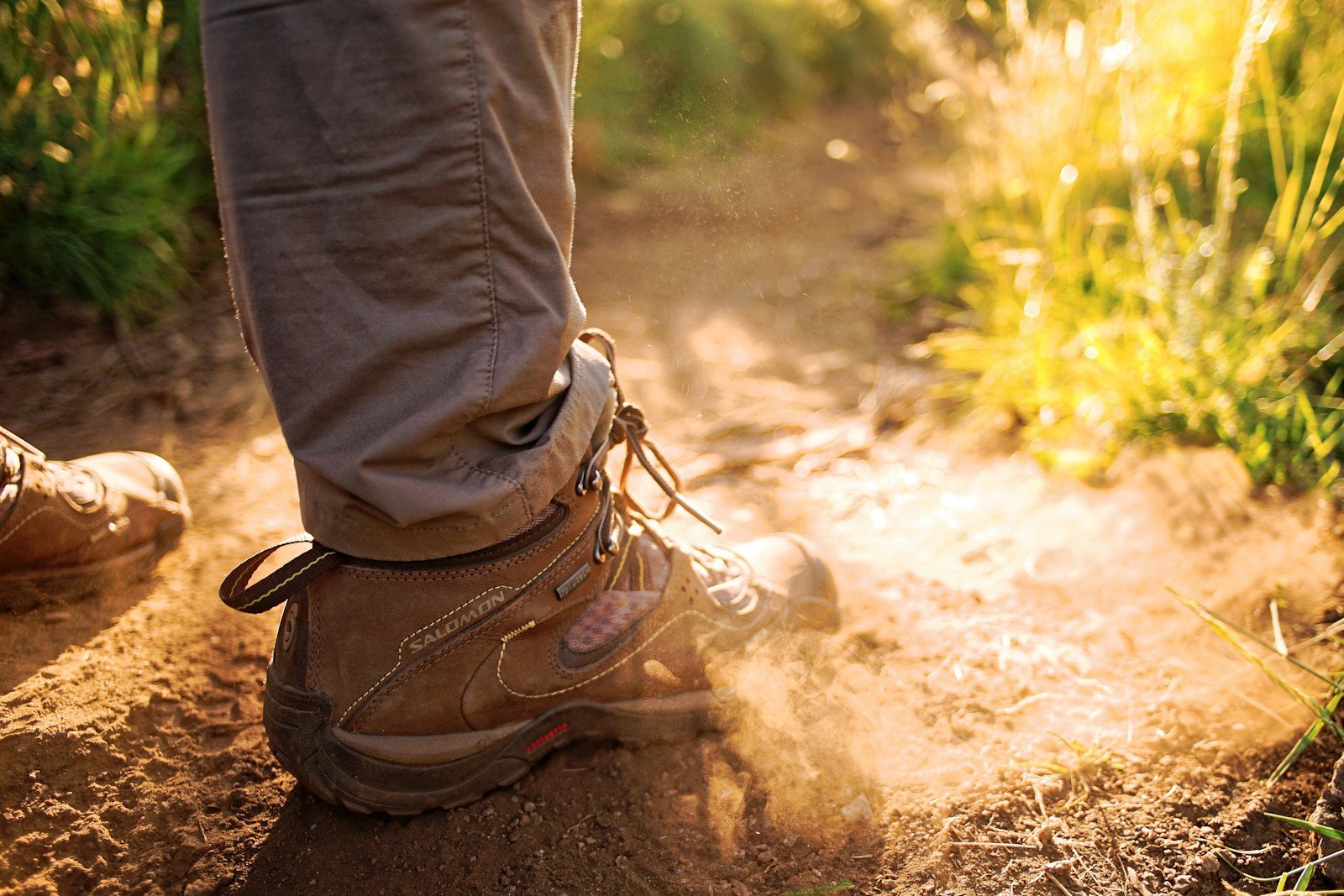 A brown hiking boot kicking up dust on a dry trail.