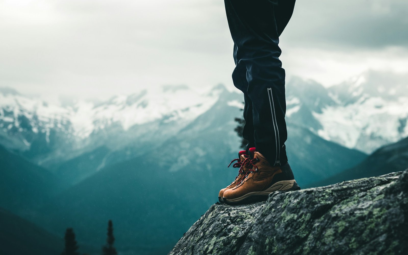 A hiker in leather boots standing on a rock above a mountain valley.