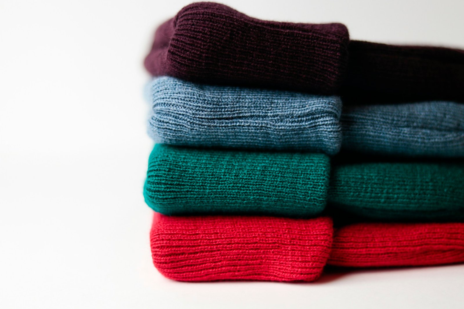 A stack of folded wool knitwear in four colours on a white background.