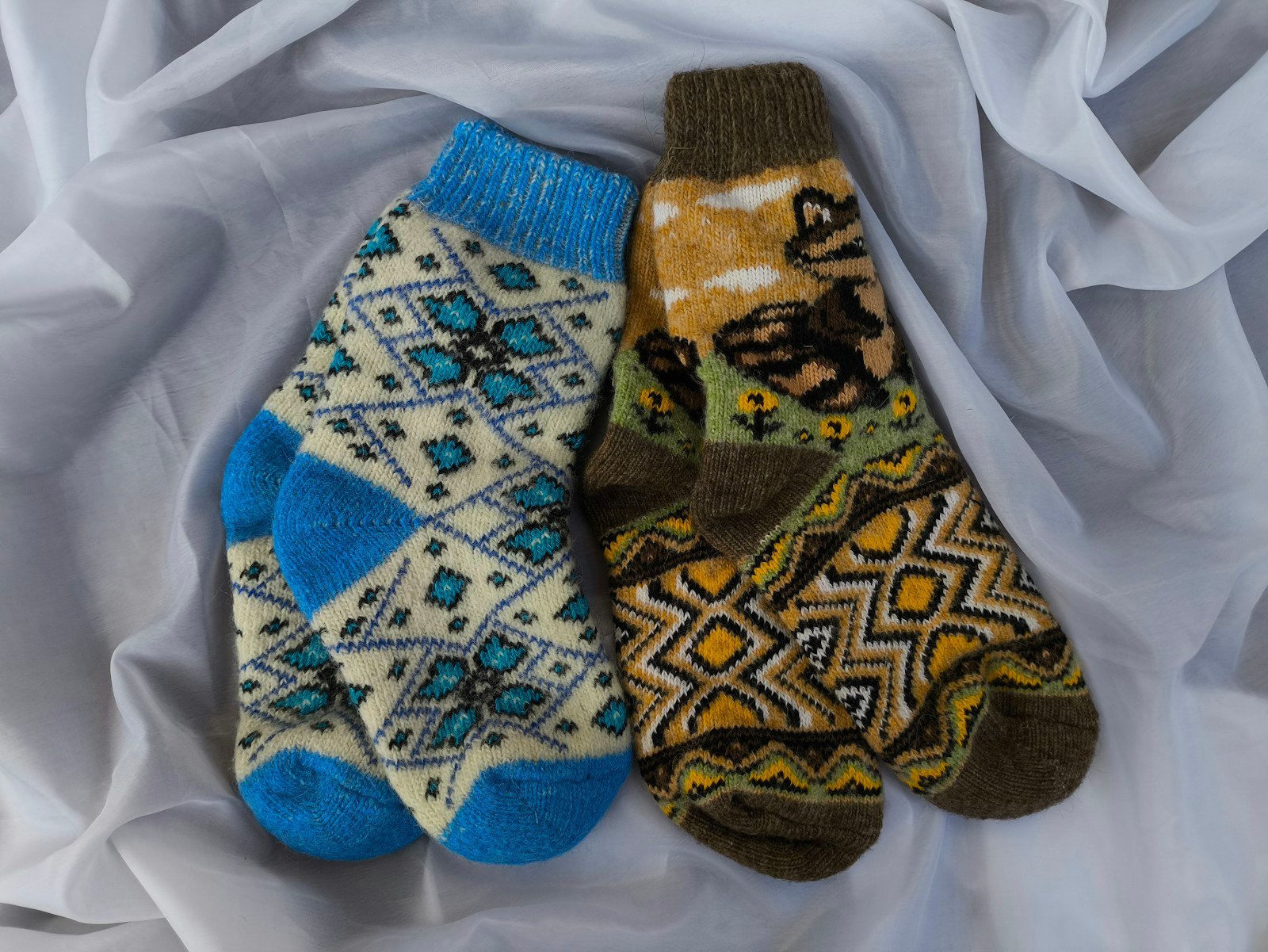 Two pairs of patterned wool socks laid out on a white sheet.