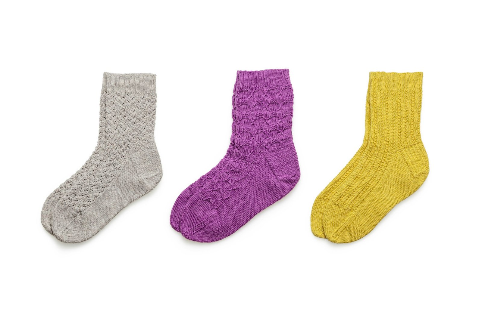 Three pairs of knitted wool socks in grey, purple and yellow on a white background.