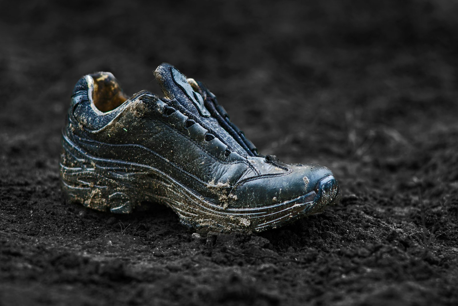 A muddy, worn trail shoe sitting on dark dirt.