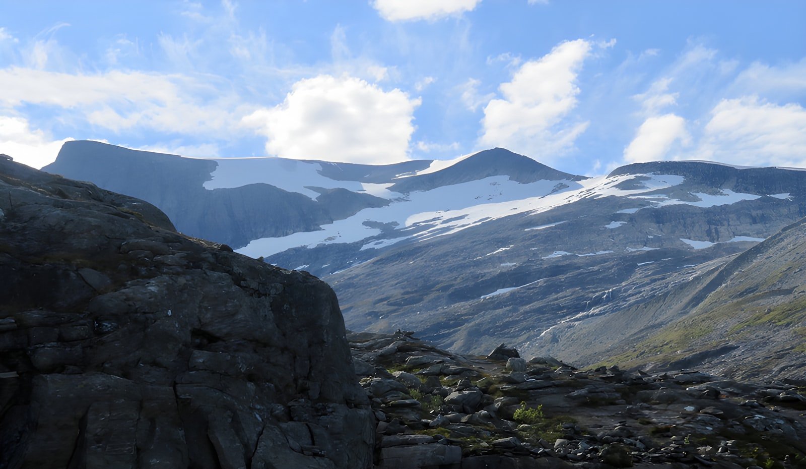 Snow-streaked Norwegian peaks under summer sky.