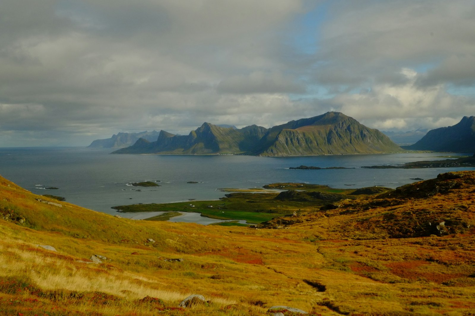 Jagged mountains rise from a calm sea under clouds.
